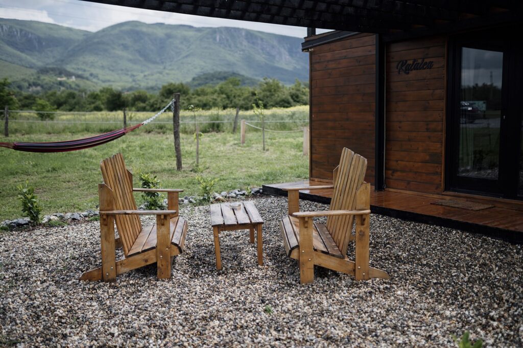 Zwei einfache Holzstühle stehen sich an einem leeren Tisch gegenüber, dahinter eine helle Wand