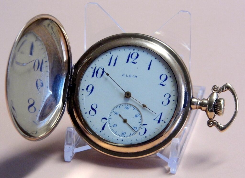 Geöffnete Taschenuhr mit römischen Ziffern und feinem Minutenzeiger liegt auf einer dunklen Unterlage