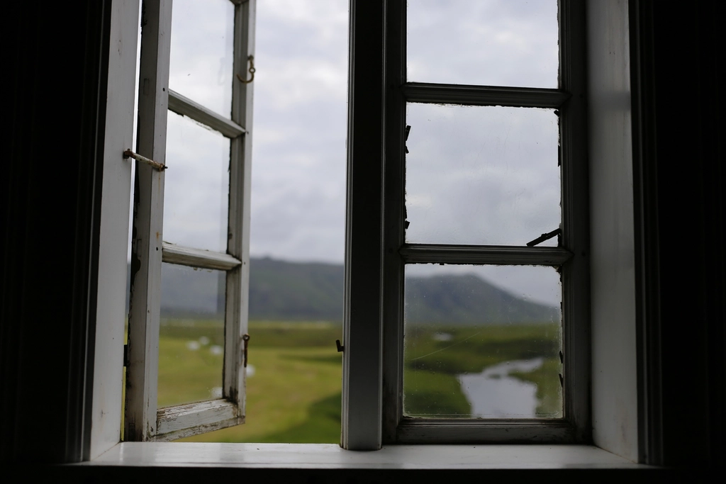 Geöffnetes Fenster mit heller Gardine, die sich leicht nach innen wölbt, dahinter Tageslicht