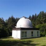 Kuppel eines Observatoriums bei Nacht mit geöffnetem Spalt und Sternen darüber